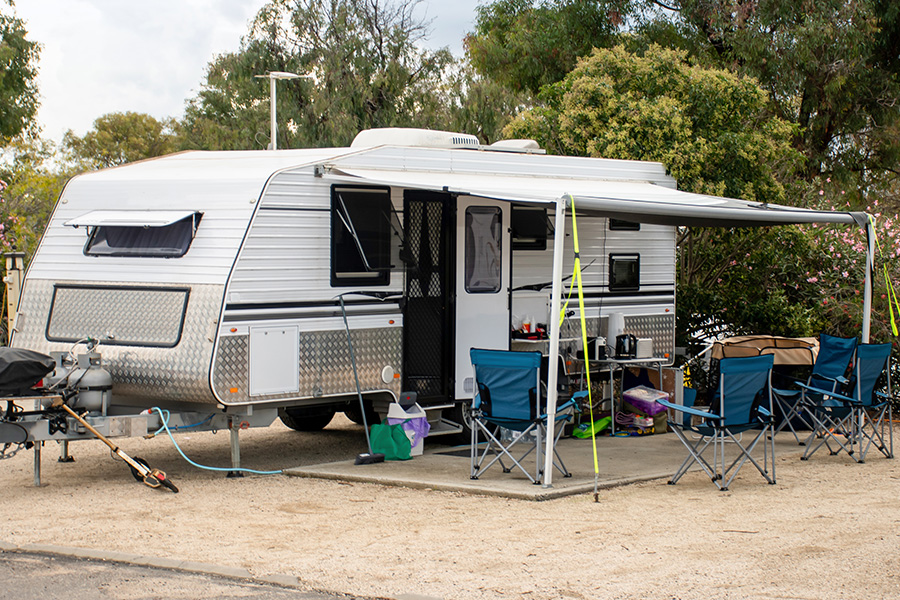 Wohnwagen mit ausgeklapptem Vorbau und Camping-Garnitur darunter auf einem Campingplatz